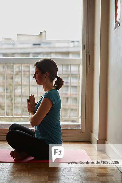 Seitenansicht einer Frau  die im Schneidersitz sitzt  die Hände zusammen in Meditation