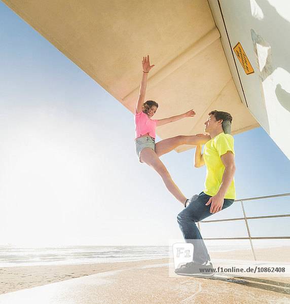 Couple practising partner yoga on beach lifeguard tower