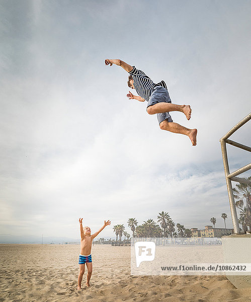 Junger Mann springt am Strand von Venice Beach,  Kalifornien,  USA,  in die offenen Arme eines Jungen