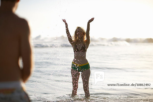 Woman in ocean wearing bikini arms raised splashing