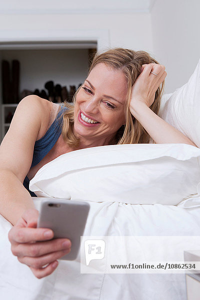 Frau liest Smartphone-Texte im Bett