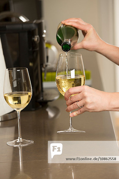Hände einer Frau  die an der Küchentheke Gläser mit Weißwein ausschenkt
