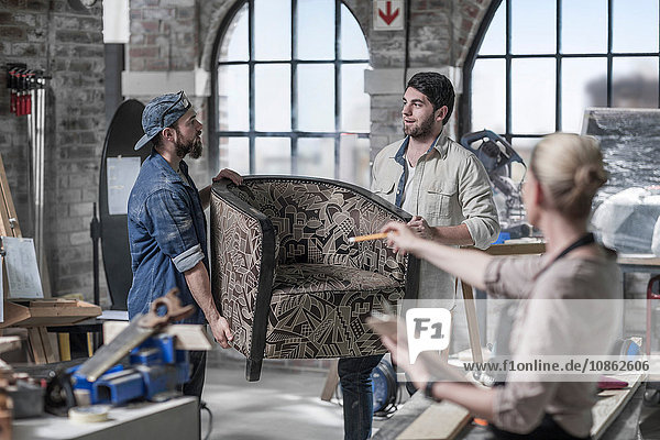 Manager leitet männliche Arbeiter  die einen Sessel in einer Antiquitäten-Restaurierungswerkstatt tragen