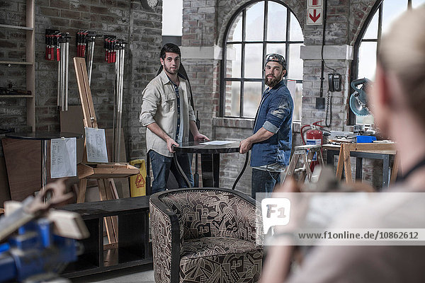 Manager leitet männliche Arbeiter  die einen Tisch in einer Antiquitäten-Restaurierungswerkstatt tragen