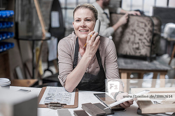 Handwerkerin im Gespräch mit einem Smartphone in einer Antiquitäten-Restaurierungswerkstatt