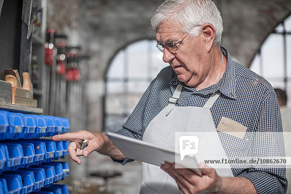 Leitender Handwerker mit digitalem Tablett bei der Auswahl von Komponenten in einer Antiquitäten-Restaurierungswerkstatt