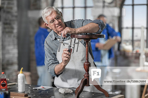 Senior-Handwerker mit Klammer auf Tisch in Antiquitäten-Restaurierungswerkstatt