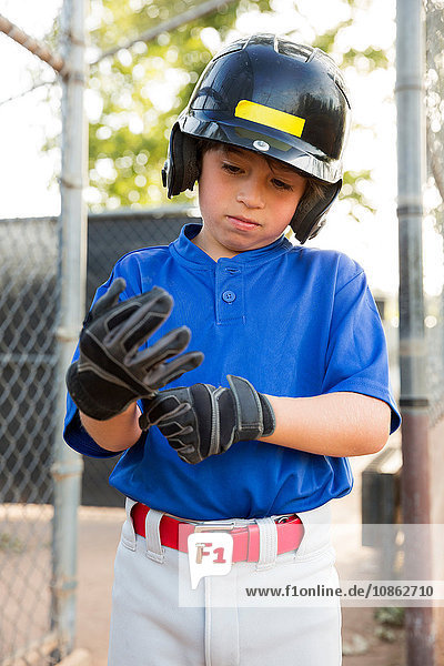 Junge zieht auf dem Baseballfeld Baseballhandschuhe an