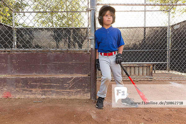 Junge lehnt mit Baseballschläger beim Training auf dem Baseballfeld gegen den Zaun