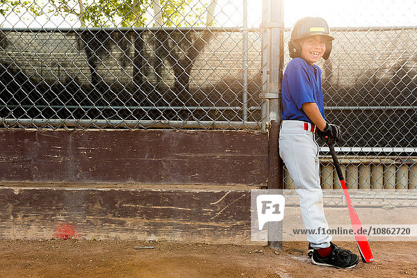 Porträt eines Jungen  der sich beim Baseball-Training gegen den Zaun lehnt