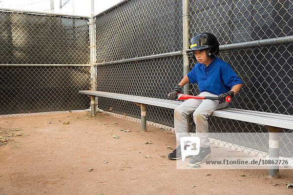 Junge mit Baseball auf Bank sitzend beim Baseball-Training