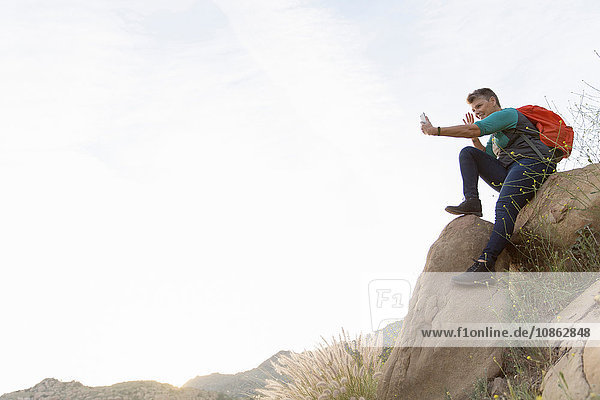 Wanderfrau sitzt auf Felsen und benutzt Smartphone zur Selbsthilfe