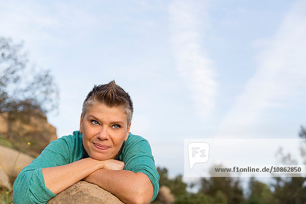 Porträt einer Frau  die sich mit den Ellbogen an einen Felsen lehnt und lächelnd wegschaut