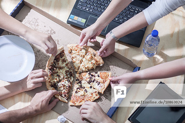 Draufsicht auf die Hände der Büroangestellten bei der Auswahl des Pizzastücks vom Schreibtisch