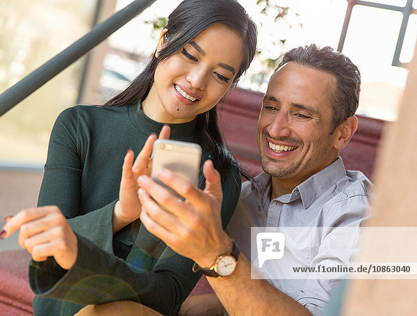 Paar sitzt auf einer Treppe und benutzt ein Smartphone und lächelt