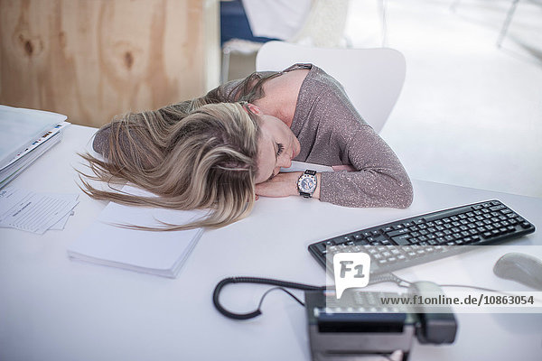Weibliche Büroangestellte schläft am Büroschreibtisch