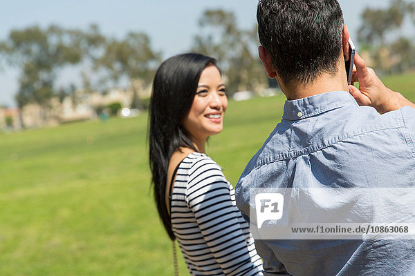 Rear view of couple using smartphone to make telephone call smiling