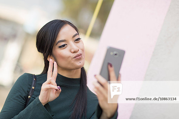 Woman doing peace sign and pouting using smartphone to take selfie