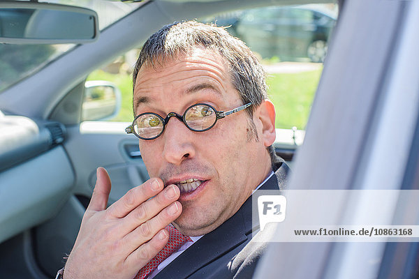 Mann im Auto mit Brille  Hand über Mund und Blick in die Kamera