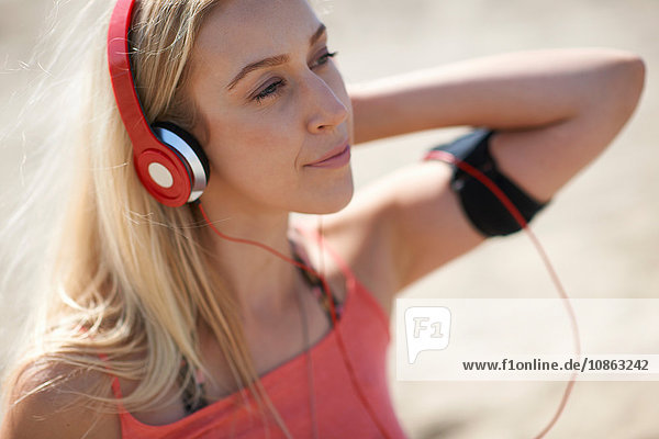 Junge Frau im Freien  mit Kopfhörern und Aktivitäts-Tracker