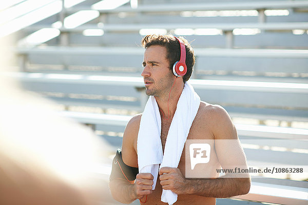 Mittelgroßer erwachsener Mann  der eine Pause vom Sport macht  Kopfhörer trägt  Handtuch um den Hals
