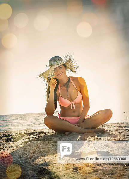 Porträt einer jungen Frau im Bikini mit gekreuzten Beinen am Strand von Miami  Florida  USA