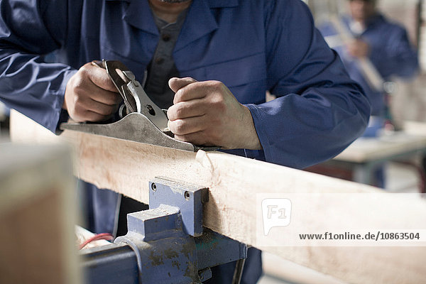Hands of carpenter using planer on plank in workshop