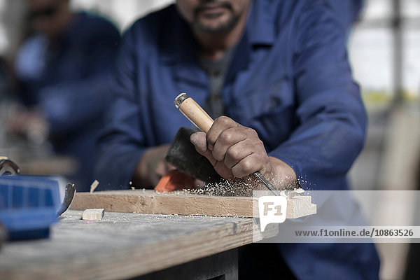 Hands of carpenter using chisel on wood in workshop