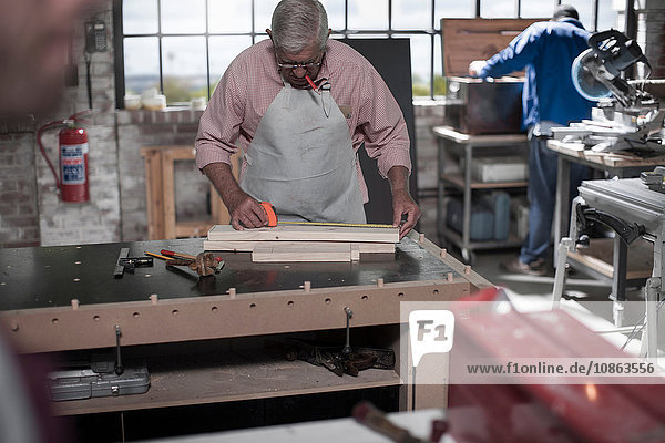 Senior carpenter measuring wood planks in workshop