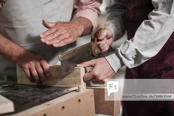 Schnappschuss eines leitenden Zimmermanns  der einem Auszubildenden in einer Werkstatt das Sägen vorführt