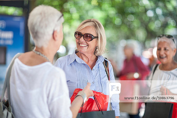 Senior woman and friend shopping and chatting in city