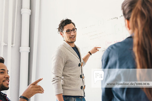 Mann vor dem Whiteboard im Gespräch mit Kollegen