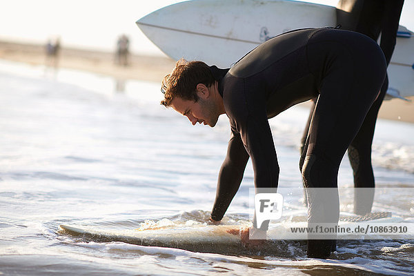 Männlicher Surfer bei der Vorbereitung eines Surfbretts im Meer am Strand von Venice Beach  Kalifornien  USA