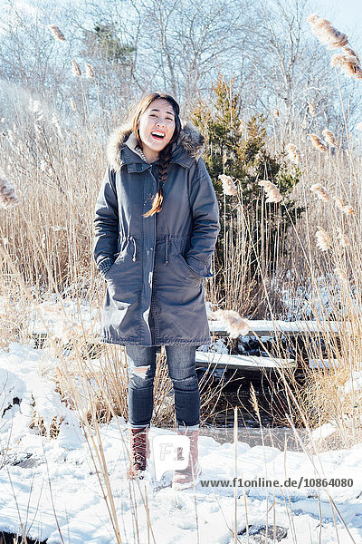 Ganzfigur einer Frau im Wintermantel in verschneiter Landschaft  die lächelnd in die Kamera blickt