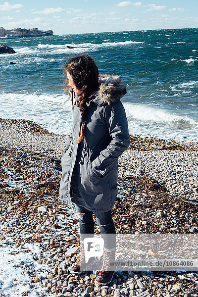 Full length view of woman on shingle beach wearing winter coat looking away