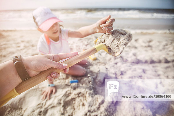 Persönliche Perspektive der Mutter am Strand  die eine Sandschaufel für ihre Tochter hält