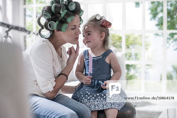 Mother in hair rollers pointing cheek to daughter