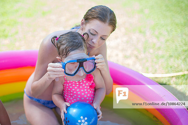 Mutter setzt der Tochter im aufblasbaren Schwimmbecken eine Schutzbrille auf