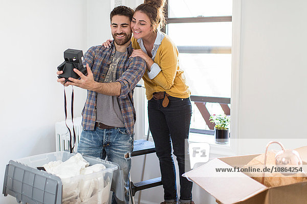 Umzug: Junges Paar beim Selbstporträt mit Sofortbildkamera
