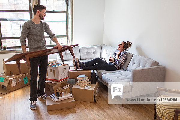 Moving house: Young woman relaxing on sofa while young man organises room