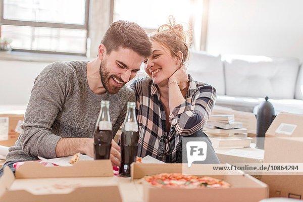 Umzug: Junges Paar isst Pizza im neuen Zuhause  umgeben von Kartons