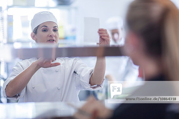 Chefkoch nimmt Bestellungen von Kellnerin in der Küche entgegen