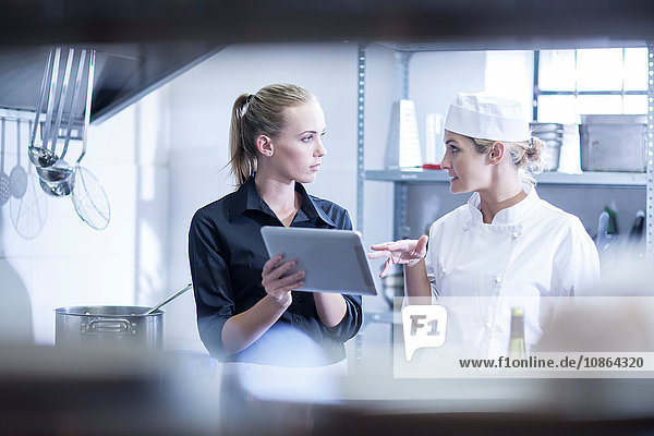Kellnerin und Koch besprechen Bestellungen auf digitalem Tablett in der Küche