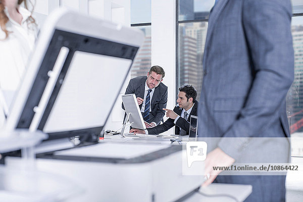 Geschäftsmann und Geschäftsfrauen unterhalten sich per Fotokopierer im Büro  Kollegen am Computer im Hintergrund