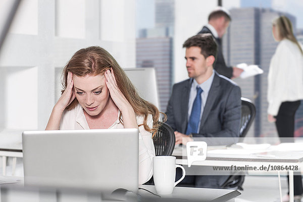 Geschäftsfrau mit Kopfschmerzen im Büro  Kollegin arbeitet im Hintergrund