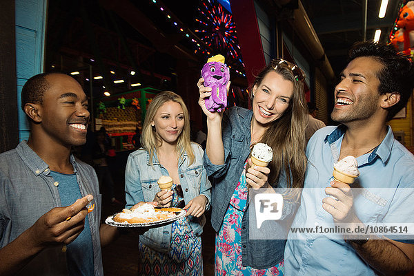 Adult friends eating ice creams in amusement park at night Santa Monica California USA