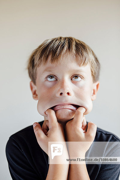Studioporträt eines Jungen, der mit den Fingern im Mund am Gesicht zieht