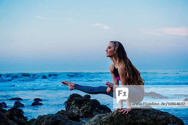 Junge Frau praktiziert Yoga-Pose auf Felsen am Strand  Los Angeles  Kalifornien  USA