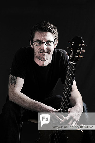 Tiefgestelltes Porträt eines Mannes im mittleren Erwachsenenalter und seiner akustischen Gitarre