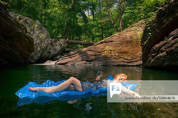 Frau hält Weinglas und entspannt sich auf einem Schlauchboot im See  Devil's Pool  Wissahickon Park  Philadelphia  U.S.A